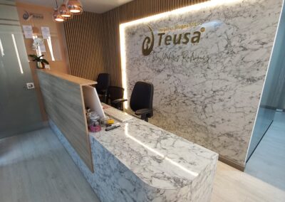 Recepción con acabados en mármol y madera que evocan elegancia, delicadeza y sofisticación. Un logo dorado en acrílico destaca en el centro de un imponente muro de impacto. La iluminación cálida, cuidadosamente integrada, aporta armonía y una sensación acogedora al espacio
