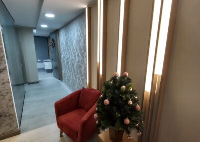 Sala de espera con poltronas terracota, paneles iluminados en madera y papel de colgadura blanco – Diseño interior por Brandinn. Elementos Destacados del Diseño: Iluminación integrada en paneles verticales, aportando calidez y modernidad. Poltronas terracota con patas de madera, que combinan elegancia y confort. Decoración con imágenes de ecografías 3D, reforzando la identidad del espacio. Pared con papel de colgadura, añadiendo un toque sofisticado.