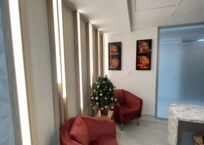 Sala de espera con poltronas terracota, paneles iluminados en madera y decoración temática con imágenes de ecografías 3D – Diseño interior por Brandinn. Elementos Destacados del Diseño: Iluminación integrada en paneles verticales, aportando calidez y modernidad. Poltronas terracota con patas de madera, que combinan elegancia y confort. Decoración con imágenes de ecografías 4D, reforzando la identidad del espacio. Mesa con acabado en mármol, añadiendo un toque sofisticado.