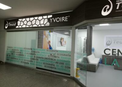 Fachada moderna de clínica ginecológica con vinilos decorativos y caja de luz led – Proyecto de diseño interior por Brandinn. Elementos Destacados del Diseño: Panel superior con iluminación y patrón geométrico, aportando modernidad y elegancia. Vinilos brush con palabras clave del sector, creando privacidad sin perder visibilidad. Branding estratégico, con logos y colores alineados a la identidad de la marca. Diseño limpio y acogedor, reforzando la experiencia premium para los clientes.
