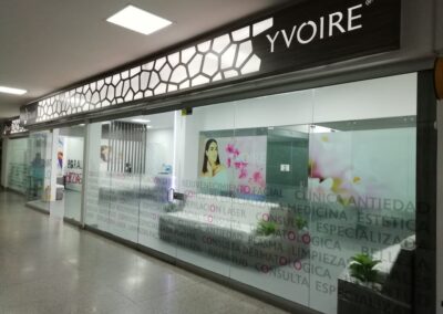 Fachada moderna de clínica de estética con vinilos decorativos y panel superior retroiluminado – Proyecto de diseño interior por Brandinn. Elementos Destacados del Diseño: Panel superior con iluminación y patrón geométrico, aportando modernidad y elegancia. Vinilos esmerilados con palabras clave del sector, creando privacidad sin perder visibilidad. Branding estratégico, con logos y colores alineados a la identidad de la marca. Diseño limpio y acogedor, reforzando la experiencia premium para los clientes.
