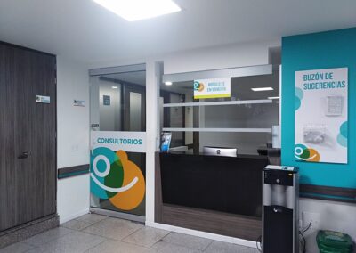 Recepción renovada con mobiliario en madera, señalética colgante y logo en acrílico con acabado brush metalizado – Proyecto de remodelación SO S.A.S. por Brandinn