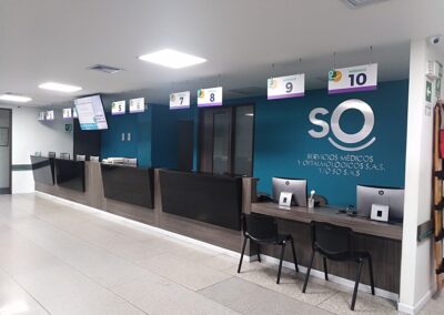 Recepción renovada con mobiliario en madera, señalización colgante y logo en acrílico con acabado brush metalizado – Proyecto de remodelación SO S.A.S. por Brandinn