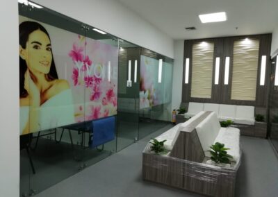 Sala de espera remodelada con mobiliario en madera, iluminación decorativa, vinilos en vidrio y jardines integrados – Proyecto de diseño interior por Brandinn. Puntos Clave del Proyecto: -Diseño moderno con tonos cálidos y texturas elegantes. -Mobiliario a medida con integración de jardines interiores. -Iluminación ambiental con paneles decorativos en pared. -Vinilos en vidrio para reforzar imagen de marca y privacidad.